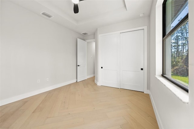 unfurnished bedroom featuring ceiling fan, a raised ceiling, a closet, and light parquet floors