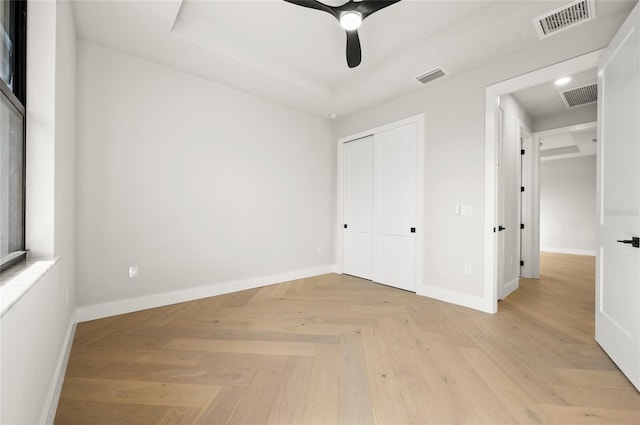 unfurnished bedroom with a tray ceiling, light parquet floors, a closet, and ceiling fan