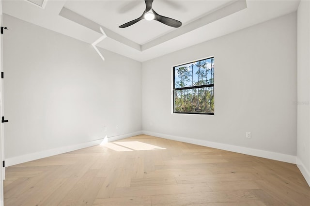 spare room with ceiling fan, a raised ceiling, and light parquet floors