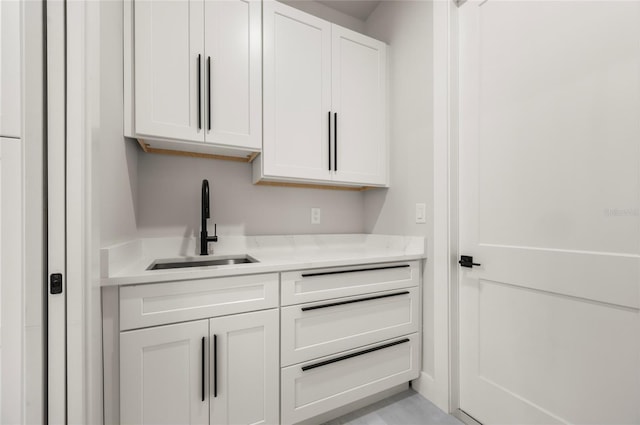 bar featuring white cabinetry, sink, and light stone countertops