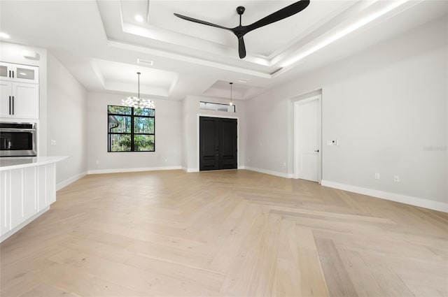 unfurnished living room with a tray ceiling, ceiling fan with notable chandelier, and light parquet flooring