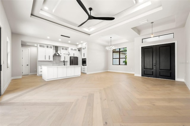 kitchen with appliances with stainless steel finishes, white cabinets, hanging light fixtures, a tray ceiling, and wall chimney exhaust hood