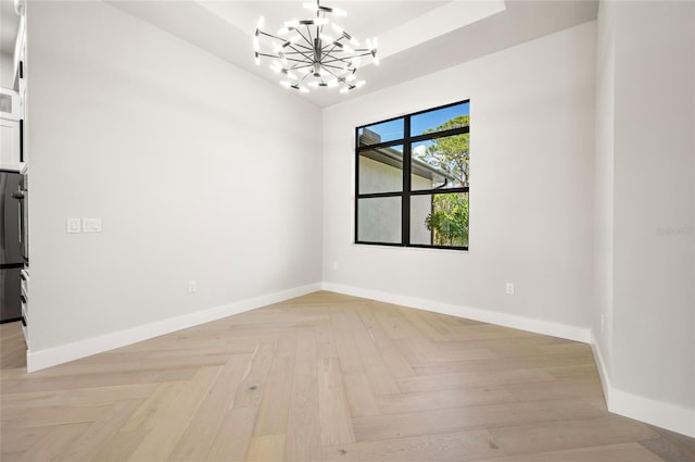 spare room featuring an inviting chandelier and light parquet flooring