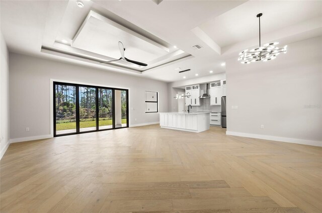 unfurnished living room with light parquet flooring, sink, an inviting chandelier, and a tray ceiling