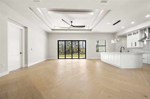 unfurnished living room featuring light parquet floors, sink, and a tray ceiling