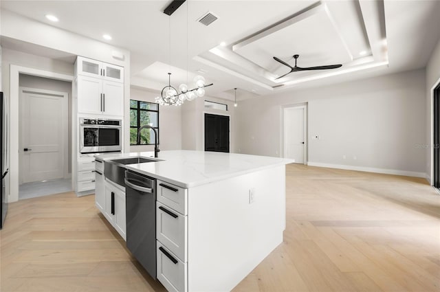 kitchen featuring a raised ceiling, white cabinetry, stainless steel appliances, light parquet flooring, and a center island with sink