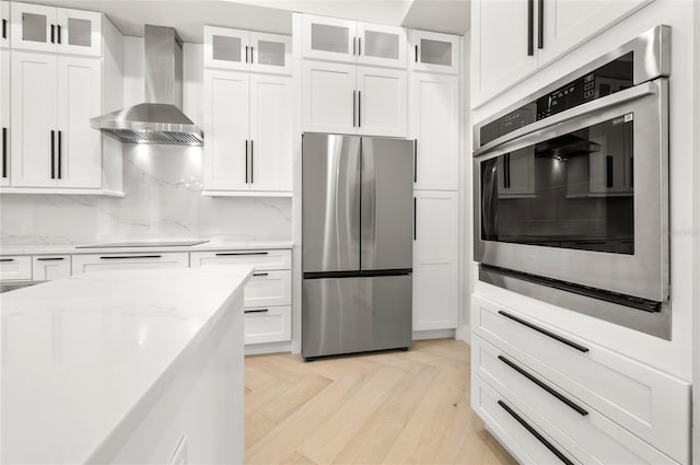 kitchen with white cabinetry, wall chimney range hood, black electric cooktop, and stainless steel refrigerator