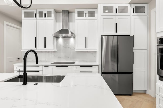 kitchen featuring white cabinetry, stainless steel appliances, light stone countertops, and wall chimney range hood