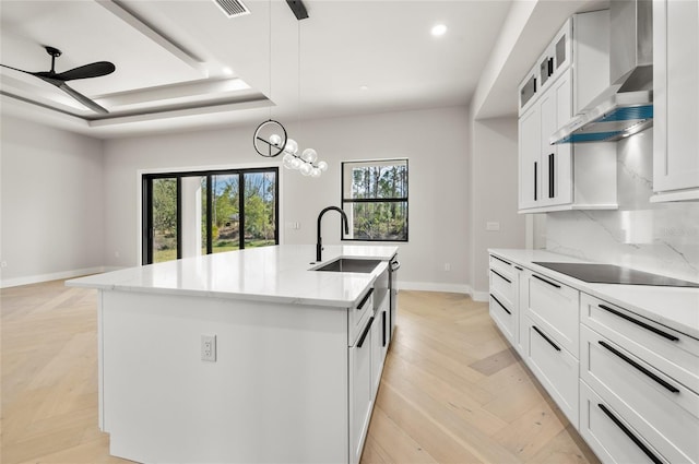 kitchen featuring wall chimney exhaust hood, sink, a raised ceiling, an island with sink, and white cabinets