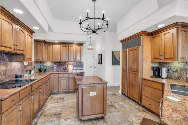 kitchen featuring a center island, backsplash, black electric stovetop, hanging light fixtures, and light stone counters