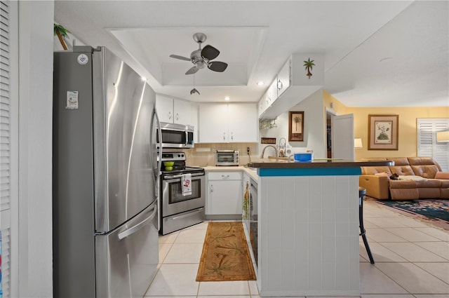 kitchen featuring kitchen peninsula, appliances with stainless steel finishes, decorative backsplash, light tile patterned floors, and white cabinetry