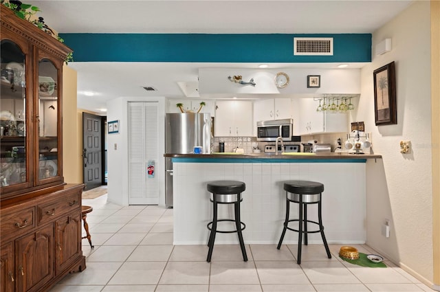 kitchen featuring stainless steel appliances, light tile patterned floors, kitchen peninsula, a kitchen bar, and white cabinets