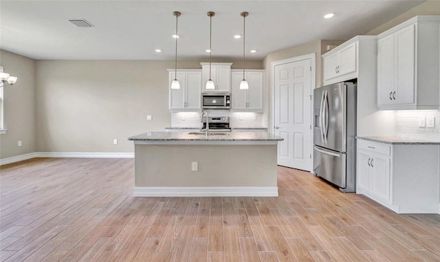 kitchen featuring decorative light fixtures, white cabinets, a kitchen island with sink, and stainless steel appliances