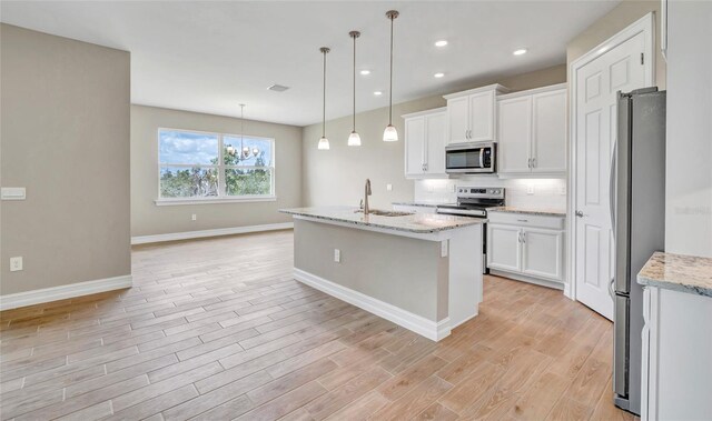 kitchen featuring decorative light fixtures, white cabinetry, appliances with stainless steel finishes, and a kitchen island with sink