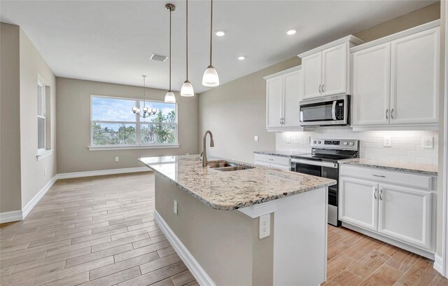 kitchen with appliances with stainless steel finishes, white cabinetry, hanging light fixtures, sink, and an island with sink