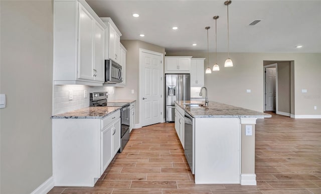 kitchen with appliances with stainless steel finishes, hanging light fixtures, a kitchen island with sink, white cabinets, and sink