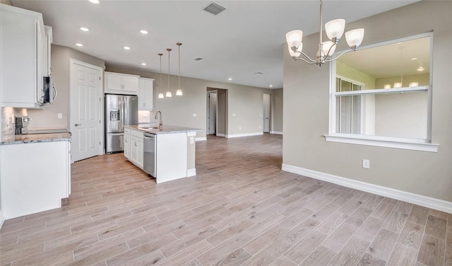 kitchen featuring pendant lighting, white cabinets, a center island with sink, and stainless steel appliances