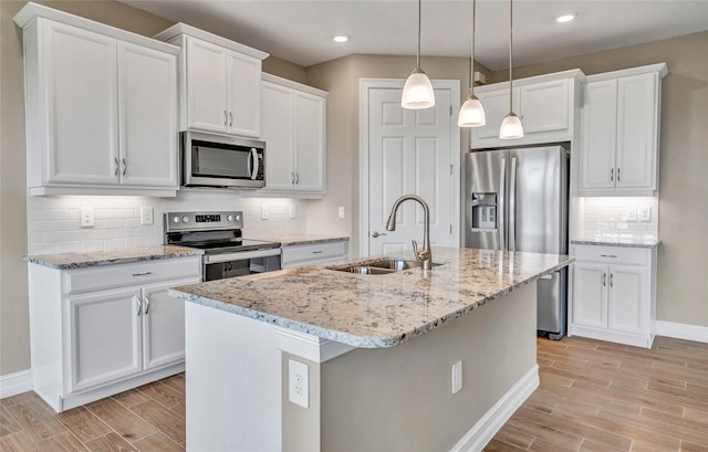 kitchen featuring pendant lighting, white cabinets, stainless steel appliances, an island with sink, and sink