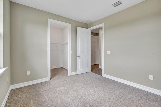 unfurnished bedroom with a closet, a spacious closet, and light carpet