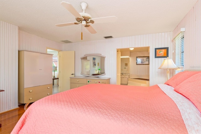 bedroom with wood finished floors, visible vents, a textured ceiling, and wallpapered walls