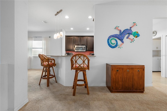 kitchen featuring light stone countertops, light carpet, a breakfast bar area, kitchen peninsula, and decorative light fixtures