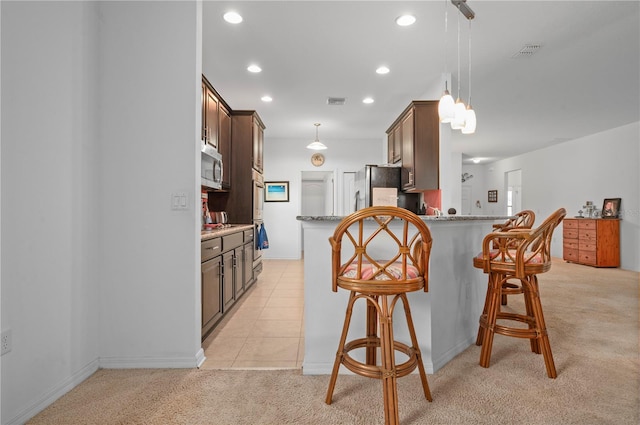 kitchen with light colored carpet, a breakfast bar area, fridge, and kitchen peninsula