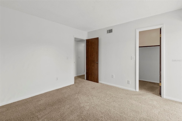 unfurnished bedroom featuring a walk in closet, light colored carpet, and a closet