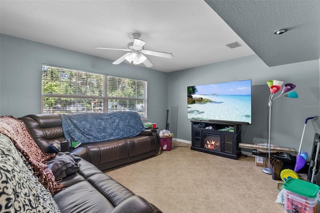 living room with ceiling fan, a fireplace, light tile patterned flooring, and a textured ceiling