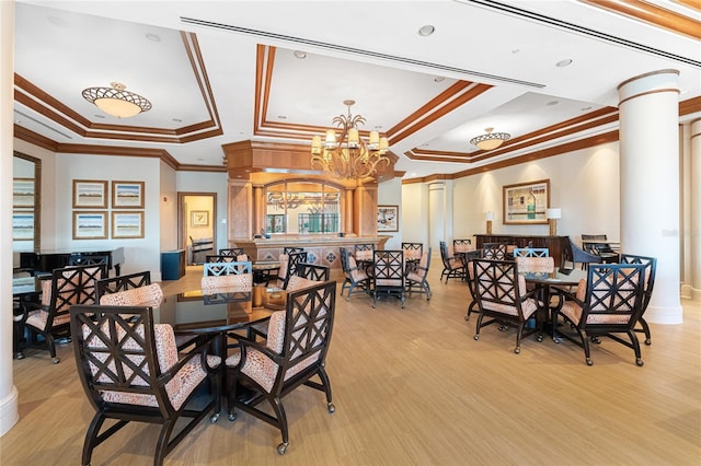 dining area with decorative columns, a chandelier, ornamental molding, a tray ceiling, and light wood-type flooring