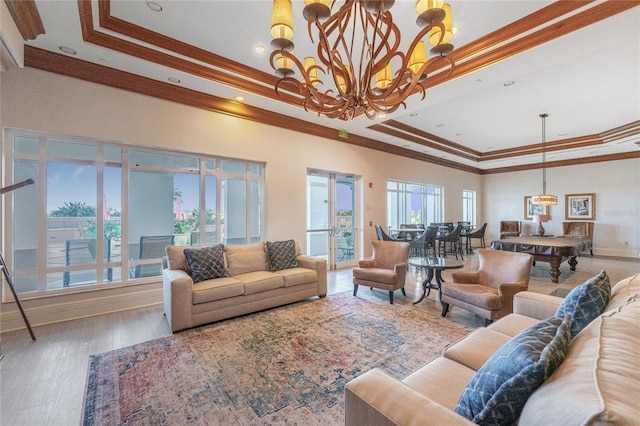 living room with hardwood / wood-style flooring, ornamental molding, an inviting chandelier, and a tray ceiling