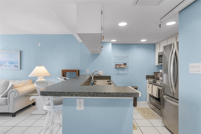 kitchen with stainless steel appliances, sink, light tile patterned floors, white cabinetry, and a breakfast bar area