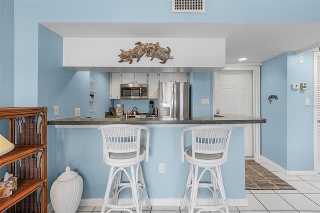 kitchen with a breakfast bar, light tile patterned floors, kitchen peninsula, and appliances with stainless steel finishes