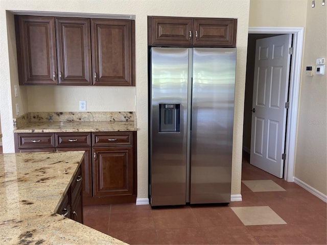 kitchen with stainless steel refrigerator with ice dispenser, dark brown cabinetry, dark tile patterned floors, and light stone counters