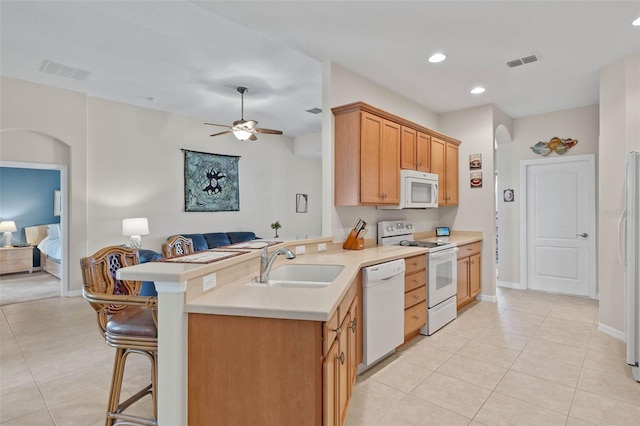 kitchen with ceiling fan, sink, kitchen peninsula, white appliances, and a breakfast bar