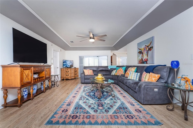 living room with a raised ceiling, ceiling fan, crown molding, and light wood-type flooring