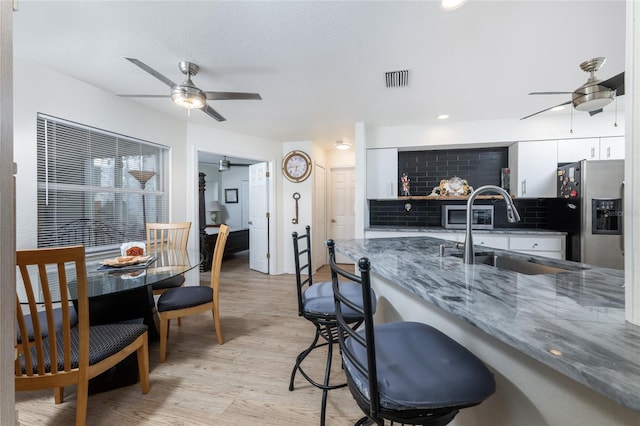 kitchen with stainless steel refrigerator with ice dispenser, sink, white cabinetry, tasteful backsplash, and dark stone counters