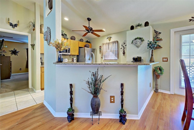 kitchen with ceiling fan, light wood-type flooring, appliances with stainless steel finishes, light stone counters, and kitchen peninsula