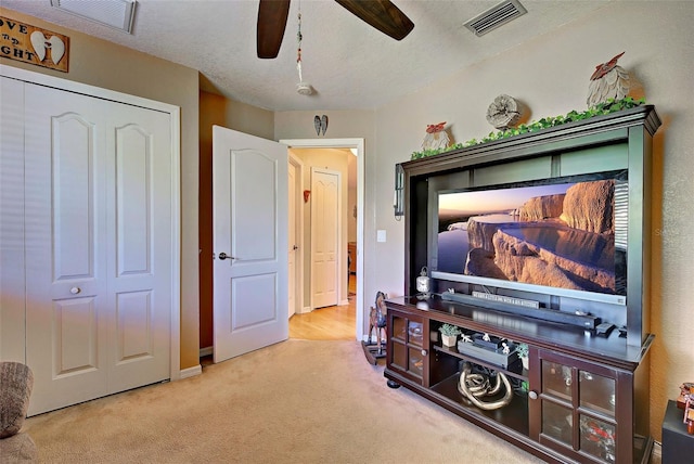 cinema room with ceiling fan, light colored carpet, and a textured ceiling