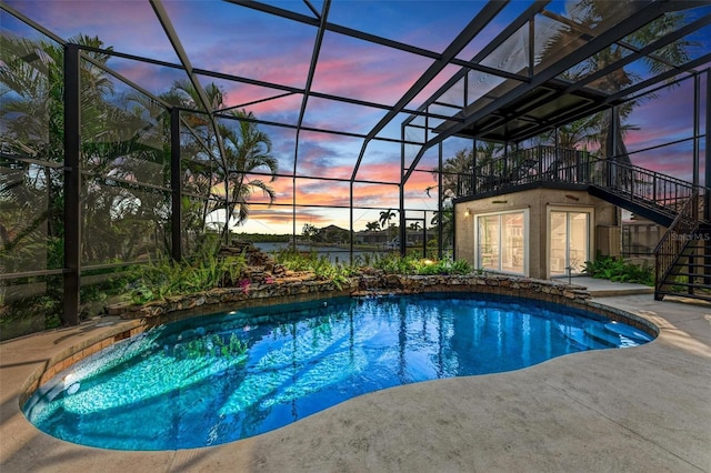 pool at dusk with glass enclosure and a patio area