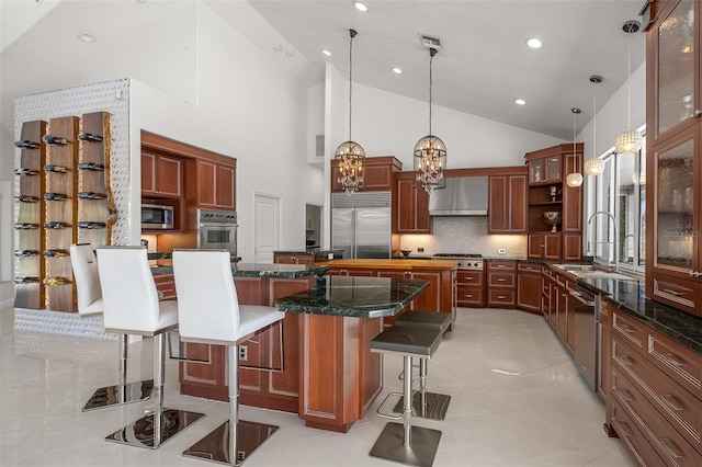 kitchen with wall chimney range hood, a kitchen island, built in appliances, light tile floors, and a breakfast bar