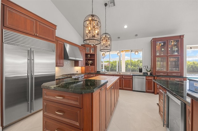 kitchen featuring light tile flooring, a notable chandelier, a kitchen island, wall chimney exhaust hood, and appliances with stainless steel finishes