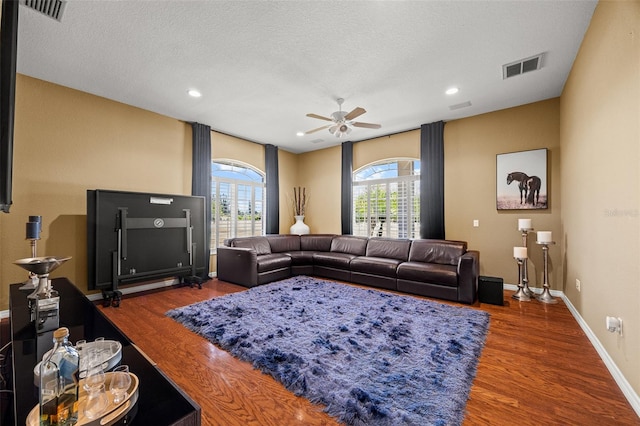 living room with a textured ceiling, dark wood-type flooring, and ceiling fan