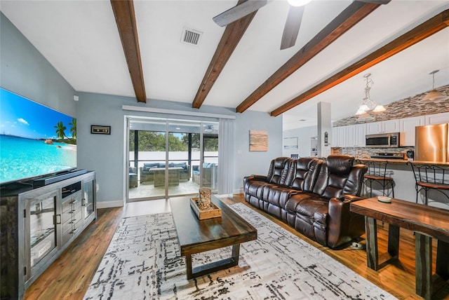 living room featuring ceiling fan with notable chandelier, lofted ceiling with beams, and light wood-type flooring