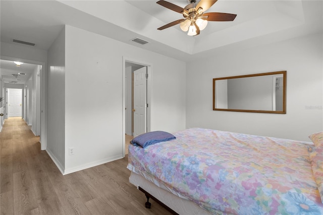 bedroom featuring light hardwood / wood-style floors, a raised ceiling, and ceiling fan