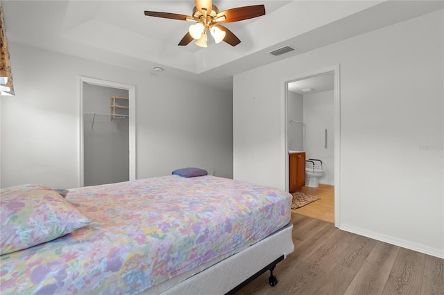 bedroom with hardwood / wood-style flooring, ceiling fan, ensuite bathroom, a raised ceiling, and a closet