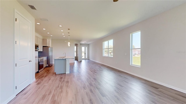 kitchen with a kitchen island with sink, white cabinets, light hardwood / wood-style flooring, decorative light fixtures, and stainless steel appliances