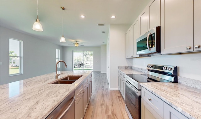 kitchen featuring ceiling fan, sink, stainless steel appliances, light stone counters, and light hardwood / wood-style flooring