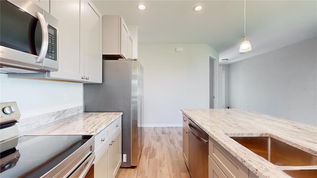 kitchen featuring appliances with stainless steel finishes, light wood-type flooring, light stone counters, and hanging light fixtures