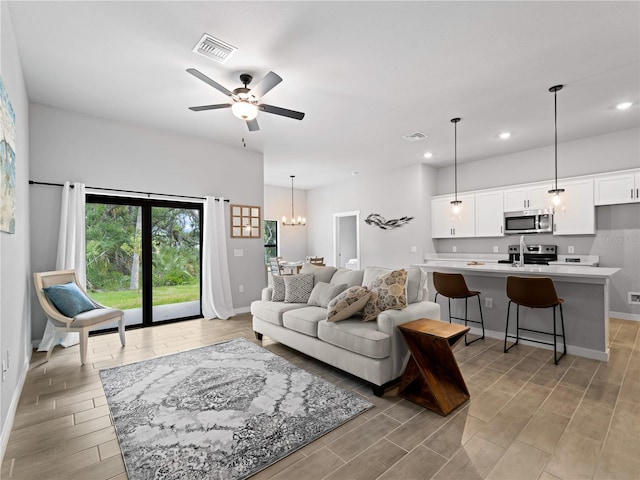 living area featuring ceiling fan with notable chandelier, wood finish floors, visible vents, and baseboards