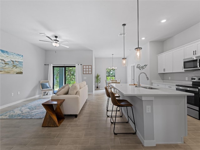 kitchen with sink, stainless steel appliances, pendant lighting, a center island with sink, and white cabinets